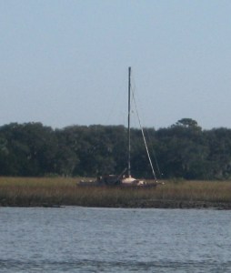 A sloop lies abandoned in the marsh.